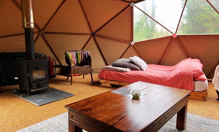 Geodome interior: woodburner, double bed, coffee table, wicker chair